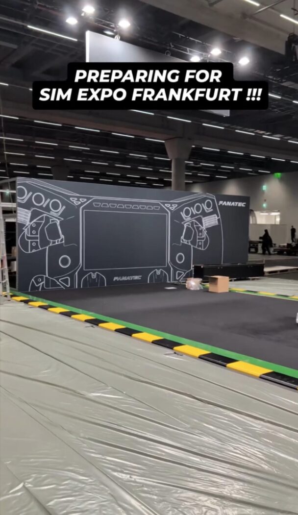 Le mur du stand Fanatec en montage à Francfort, avec un volant dessiné au trait blanc et un grand rectangle central, sous la légende Preparing for Sim Expo Frankfurt