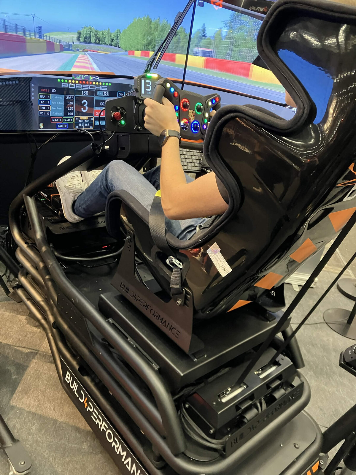 Un pilote au volant du VPG Porsche 911 GT3 R Evo, sur un cockpit Build4Performance du stand VPG, avec le circuit de Spa à l'écran