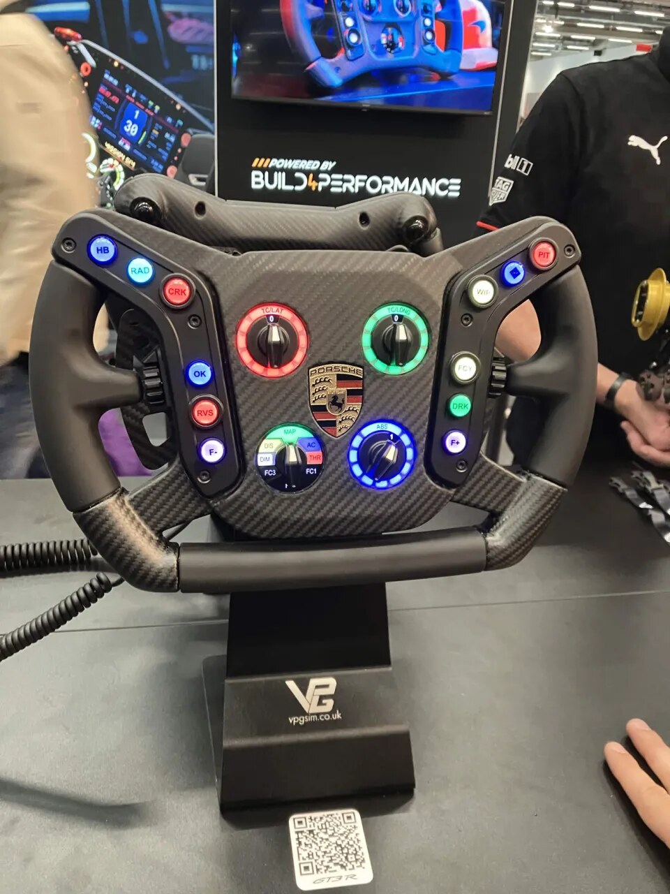 Le volant VPG Porsche 911 GT3 R Evo exposé sur le stand VPG à la SimRacing Expo 2026, boutons et molettes allumés